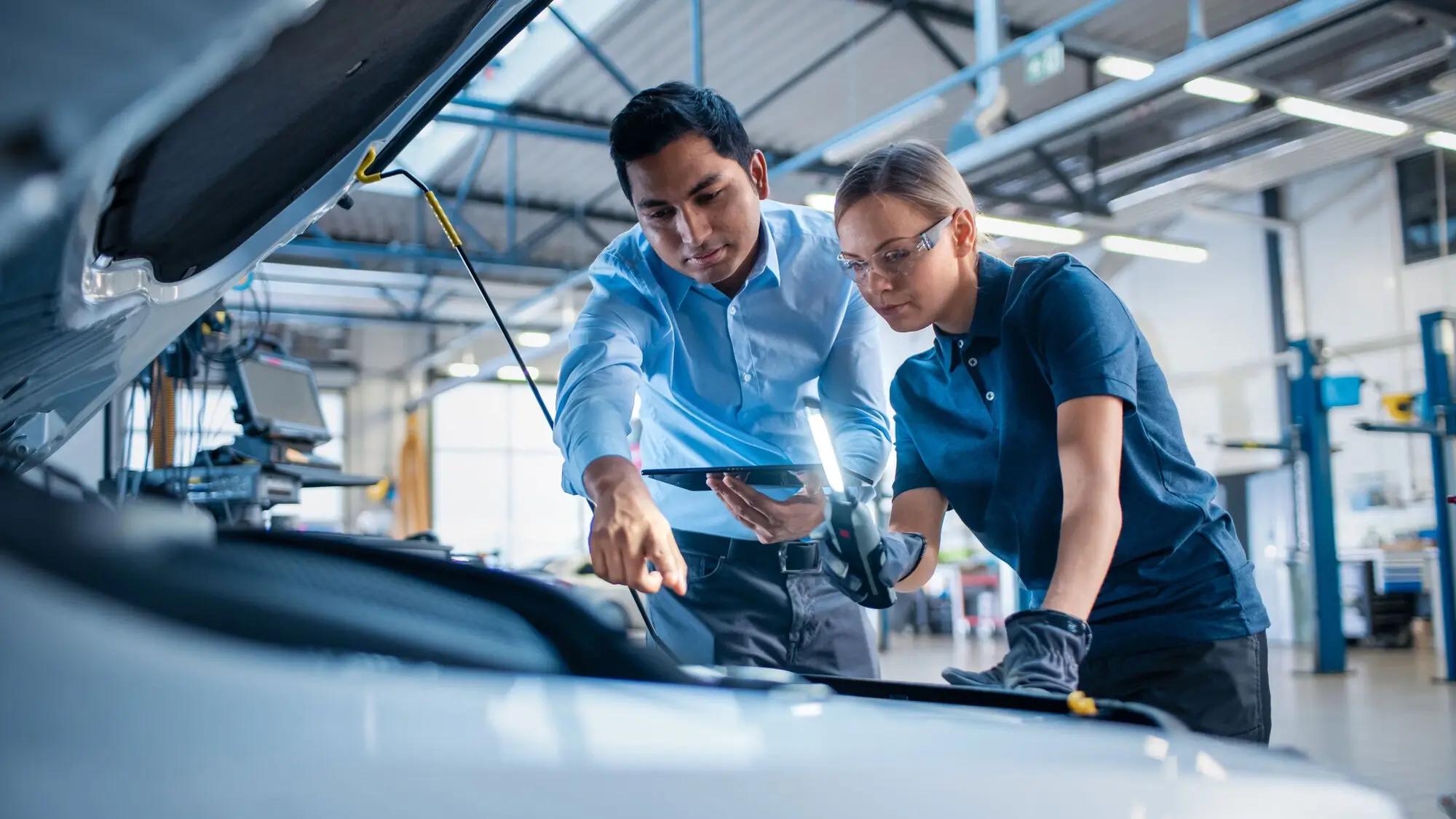 Two employees looking under the hood of a car in the automotive supply chain industry.