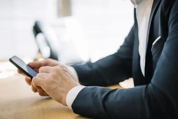 Man in a suit holding a phone to send automated invoices using advanced returnable asset management software.